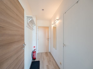 A hallway with wooden flooring, a fire extinguisher, a door, and a wall-mounted light fixture. - Studio on the 5th Floor With a Beautiful View (Middelkerke)