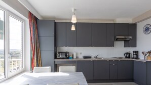 A modern kitchen with grey cabinets, a microwave, a coffee maker, and a sink. There's a dining table with chairs and a window with curtains. - Studio on the 5th Floor With a Beautiful View (Middelkerke)