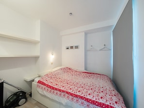 A bedroom with a bed, a bedside table, a wall-mounted light, and a vacuum cleaner. - Studio on the 5th Floor With a Beautiful View (Middelkerke)