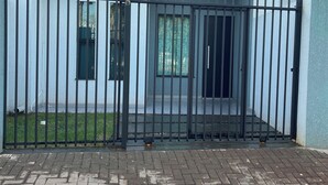 A modern building with a gated entrance, a small window, and a visible air conditioning unit. - Casinha33, O Aconchego da Tríplice Fronteira! (Jardim Cataratas Foz do Iguaçu)