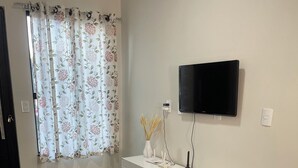 A modern living room with a grey sofa, a white console table, a flat-screen TV mounted on the wall, and a patterned rug. - Casinha33, O Aconchego da Tríplice Fronteira! (Jardim Cataratas Foz do Iguaçu)