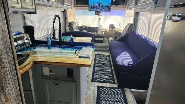 A compact RV interior with a kitchenette, a seating area, and a television. - The Holy Mackerel 
Family and pet friendly  (Perry)