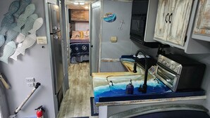A compact RV interior with a kitchenette, a bed, and a bathroom. - The Holy Mackerel 
Family and pet friendly  (Perry)