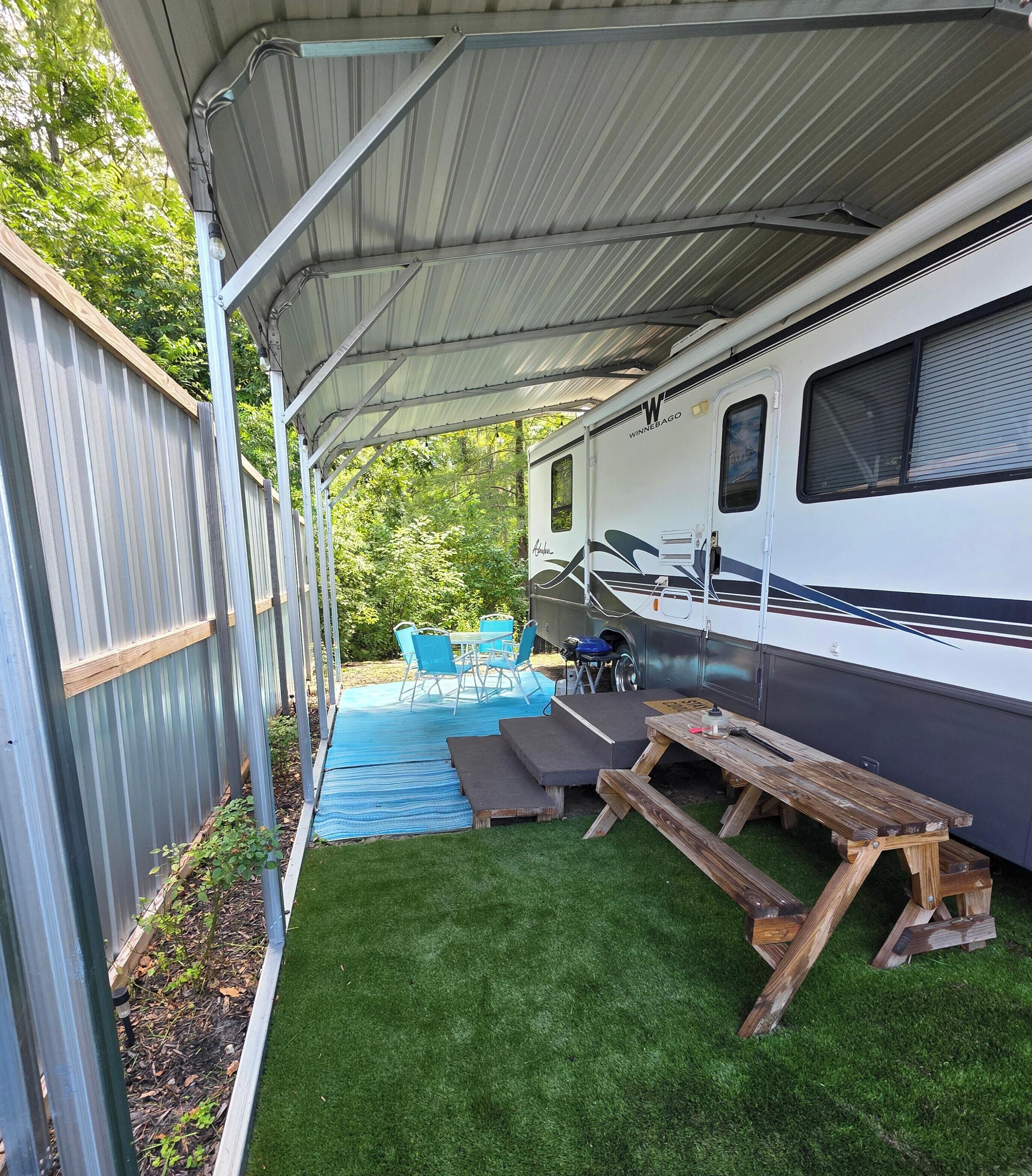 A covered outdoor area with a picnic table, a small pool, and a camper RV.