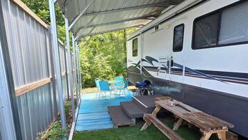 A covered outdoor area with a picnic table, a small pool, and a camper RV.