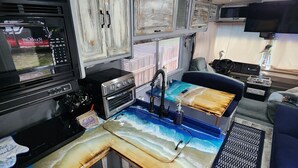 A compact kitchen with a stove, microwave, and sink. There is a small seating area with a couch and a TV mounted on the wall. - The Holy Mackerel 
Family and pet friendly  (Perry)