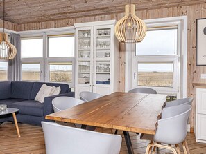 A room with a wooden dining table, white chairs, a blue sofa, and a cabinet with glassware.