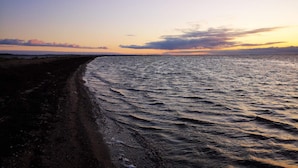 Une plage au rivage incurvé, avec une eau calme et un ciel au coucher du soleil.