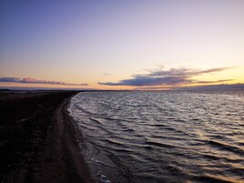 En strand med en bugtet kystlinje, stille vand og en solnedgangshimmel.