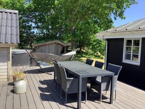 En utomhusveranda med ett bord och stolar, en hängmatta och en träkonstruktion.