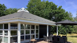 A covered patio with a grill and seating area, surrounded by a brick patio and a grassy lawn.