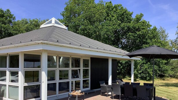Une terrasse couverte équipée d’un barbecue et d’un espace salon, entourée d’une terrasse en briques et d’une pelouse.