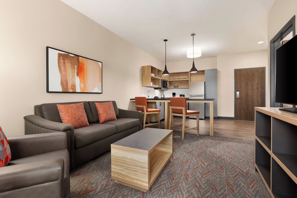 Una sala de estar moderna con un sofá, una mesa de centro y un mueble para televisión. Hay una zona de cocina con armarios y un microondas.