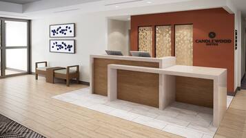 A modern reception desk with a wooden finish, two framed abstract artworks on the wall, and a sign for Candlewood Suites.