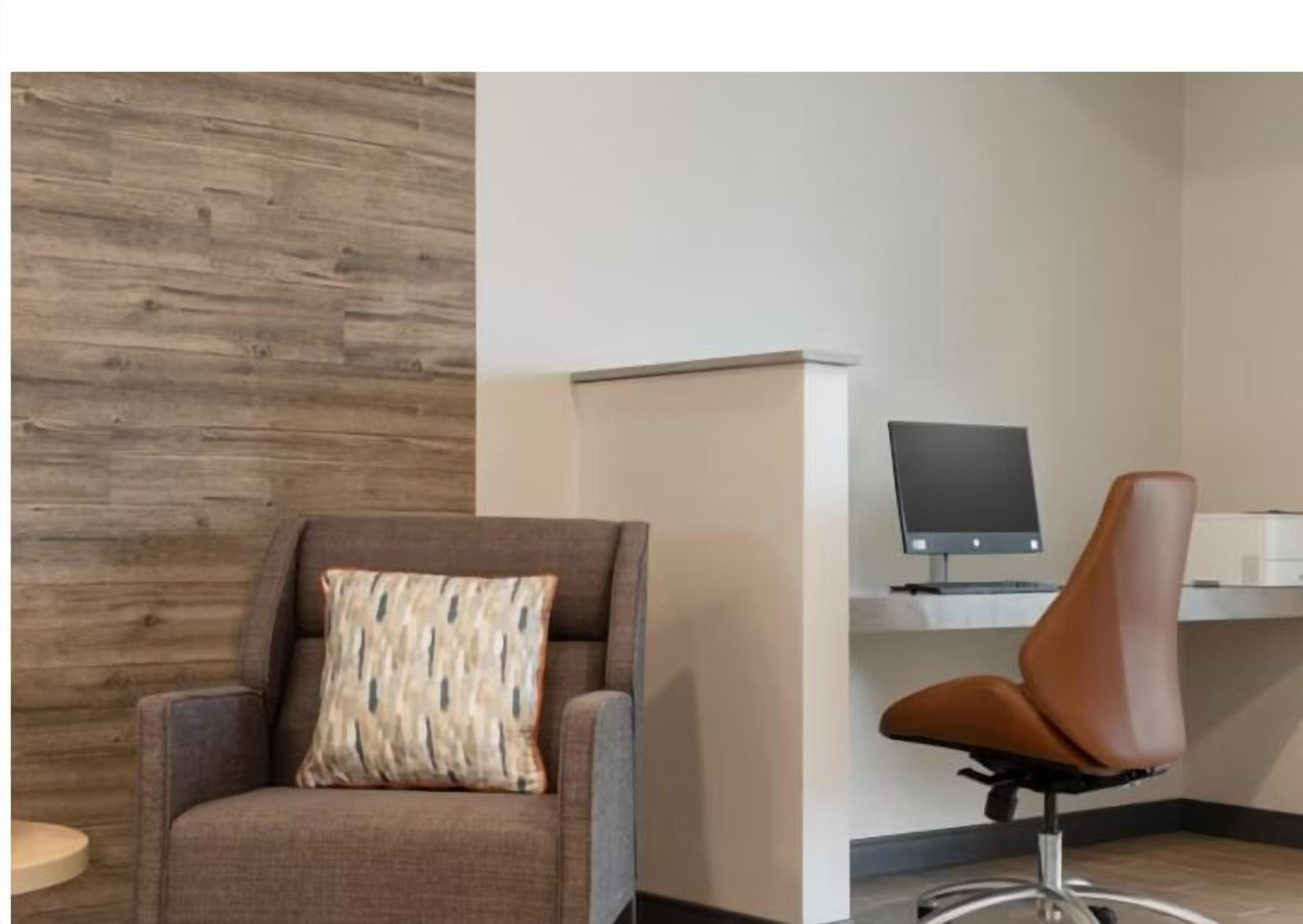 A modern office space with a brown leather chair, a cushioned armchair, and a desk with a computer monitor.