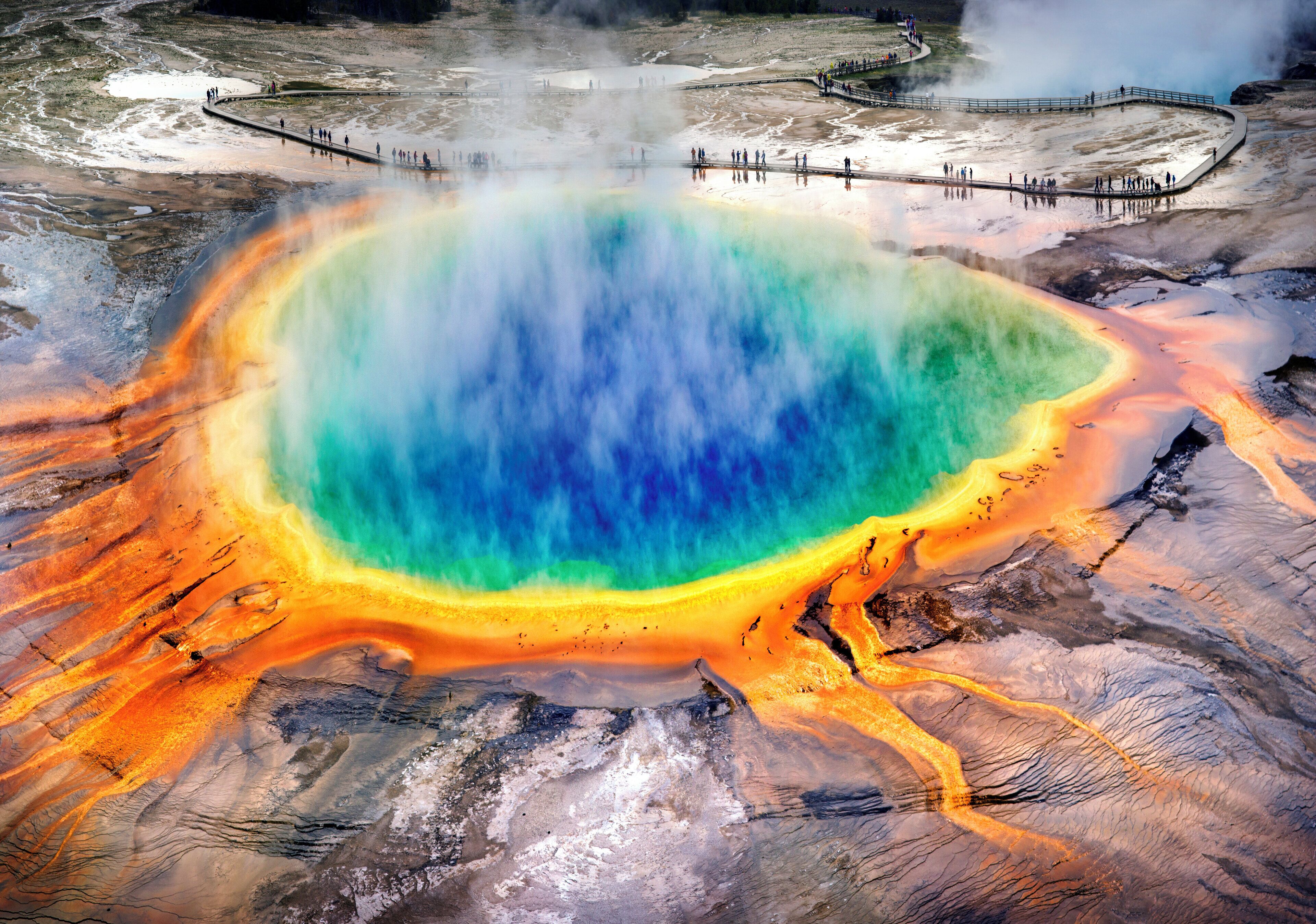A geothermal hot spring with a colorful gradient from blue to orange, surrounded by a rocky terrain.