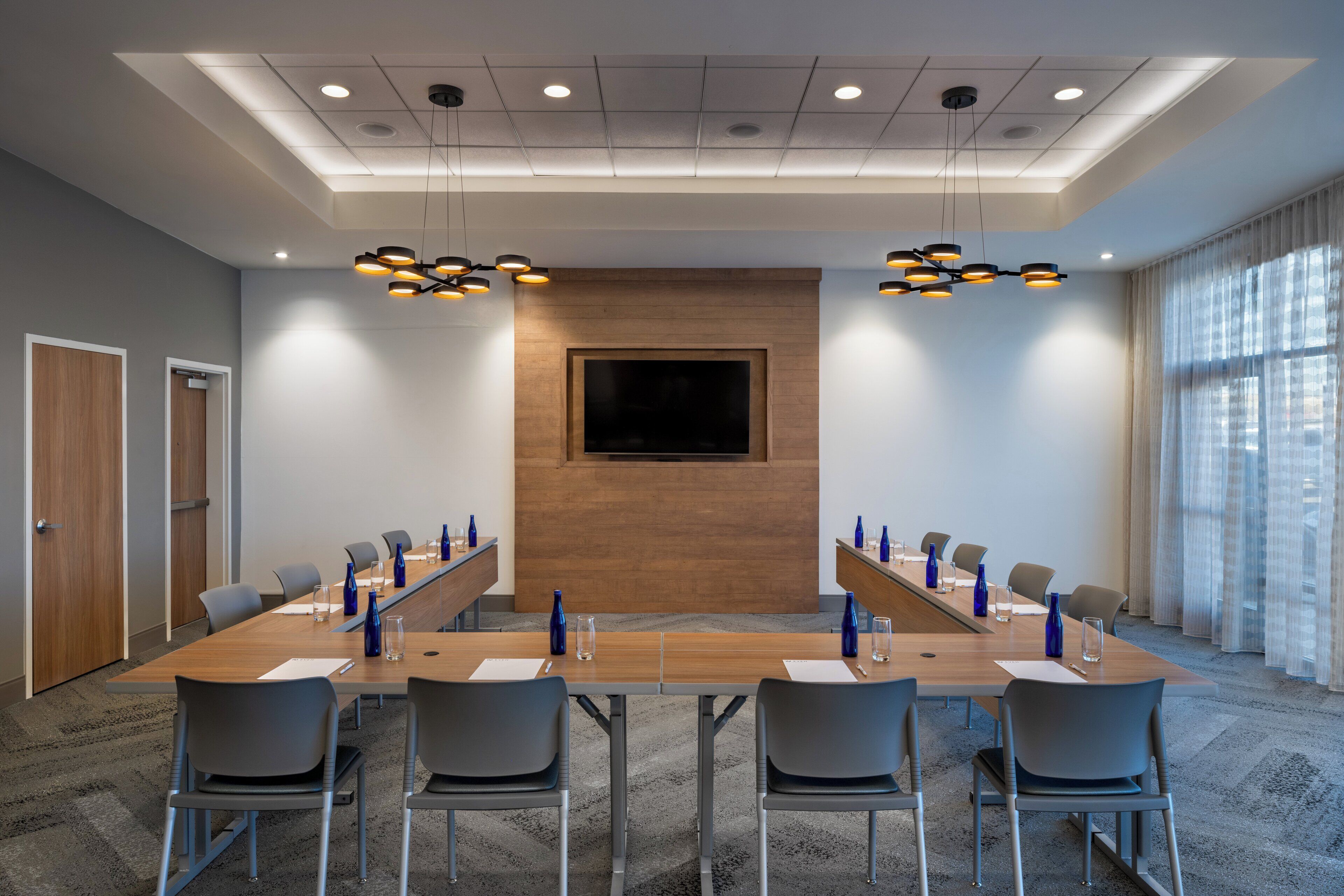 A conference room with a long table, chairs, a flat-screen TV, and pendant lighting.