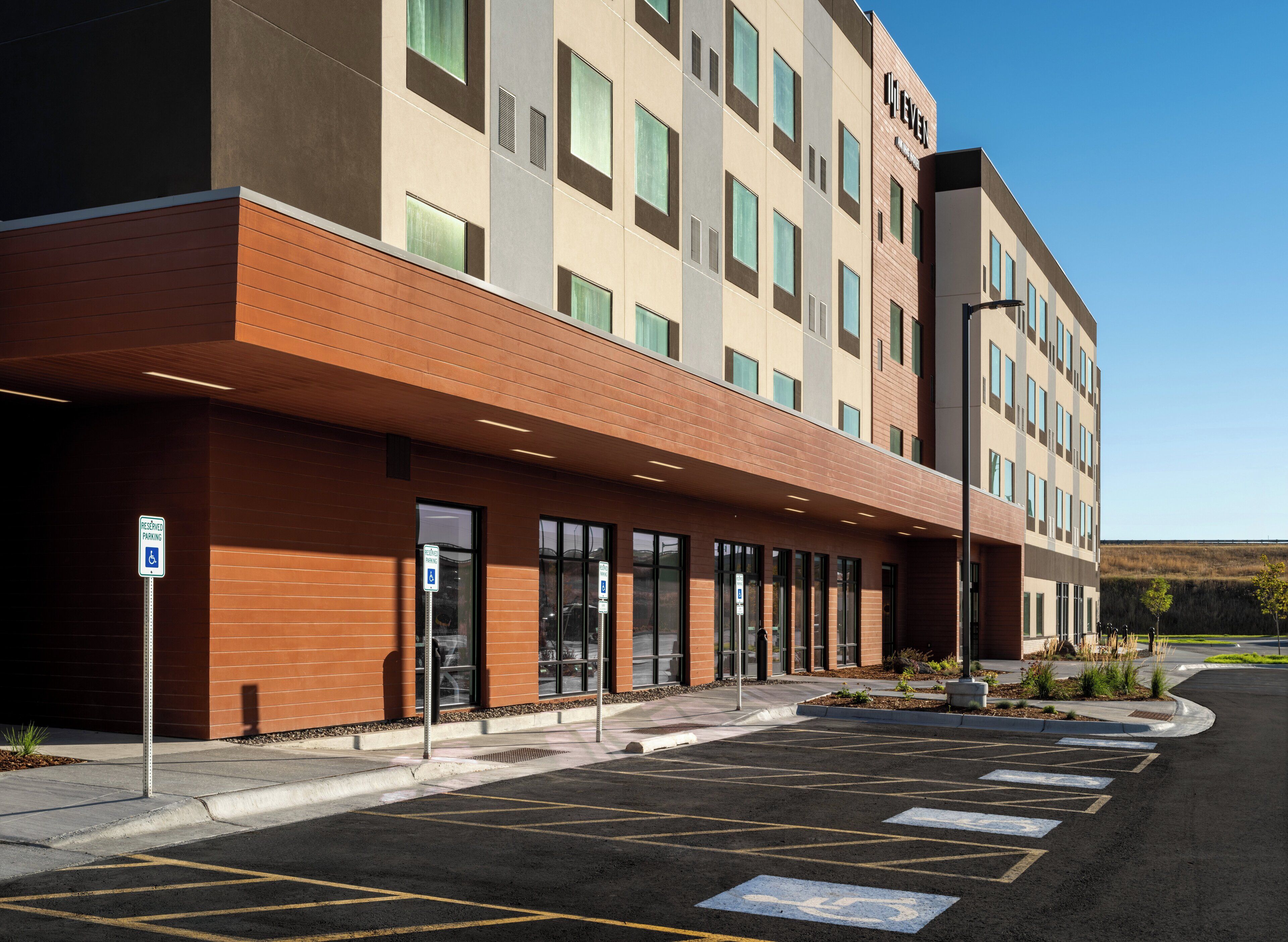A modern hotel with a brick facade, large windows, and a parking lot with designated handicapped spaces.