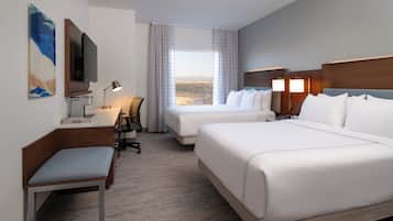 Ett hotellrum med två sängar, ett skrivbord, en stol, en TV och ett fönster med utsikt.