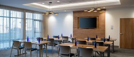 A conference room with tables, chairs, and a large screen.