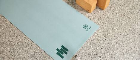Un tapis de yoga orné d’un logo, deux blocs de mousse et une bouteille d’eau, le tout posé sur un sol texturé.