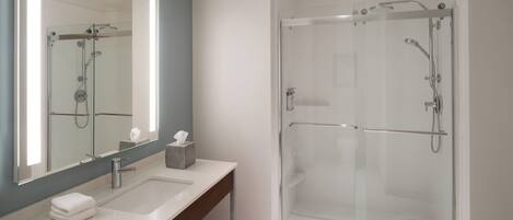 A modern bathroom with a glass-enclosed shower, a large mirror, and a vanity with towels.