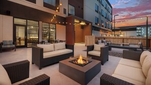 Un área de lounge al aire libre, moderna, con mobiliario de mimbre, una chimenea central e iluminación con luces colgantes.