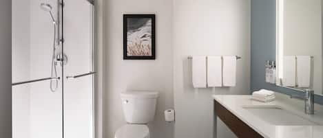 Un baño moderno con ducha acristalada, inodoro, lavamanos con espejo y un cuadro en la pared.