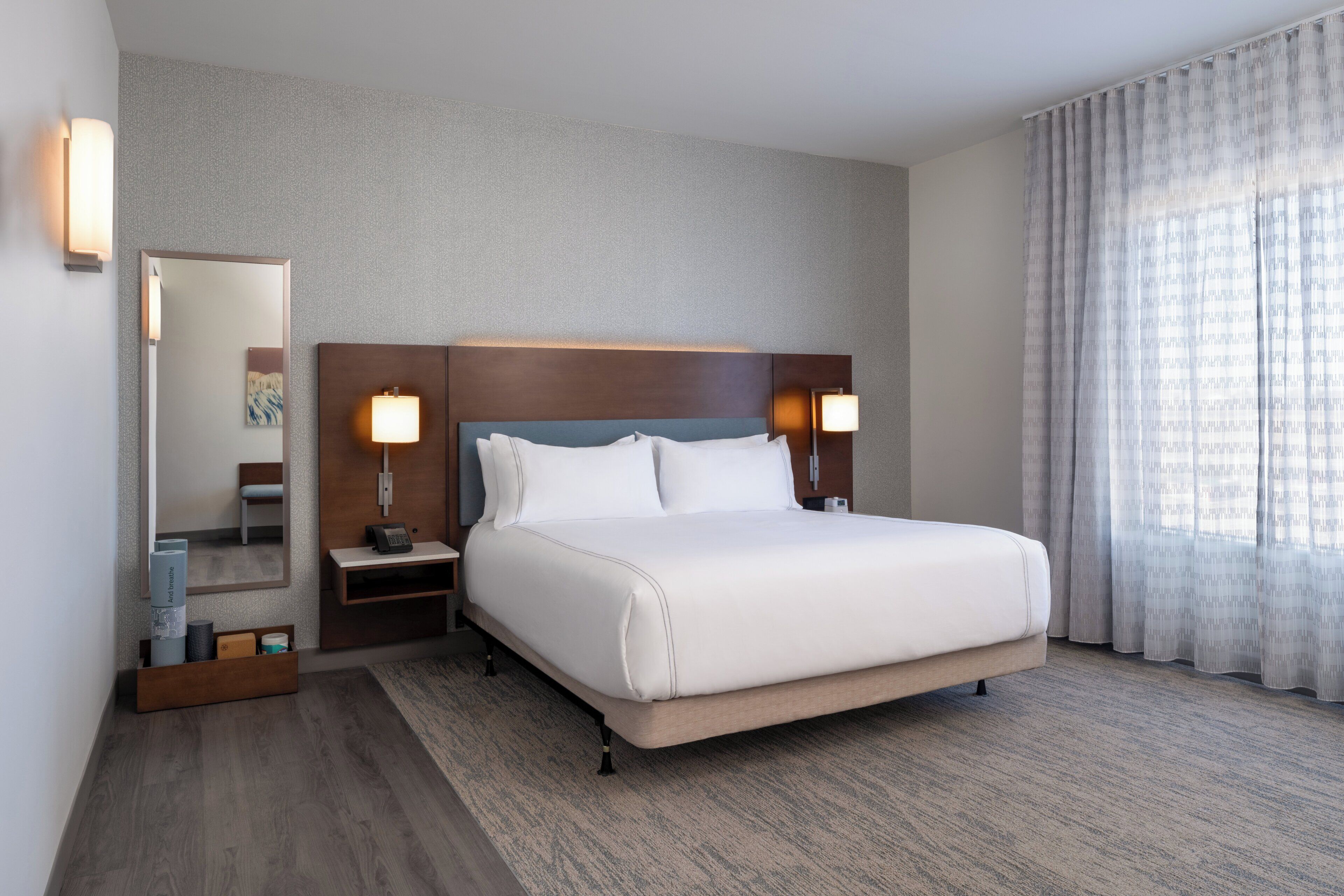 A hotel room with a large bed, two bedside tables with lamps, a mirror, and a window with curtains.