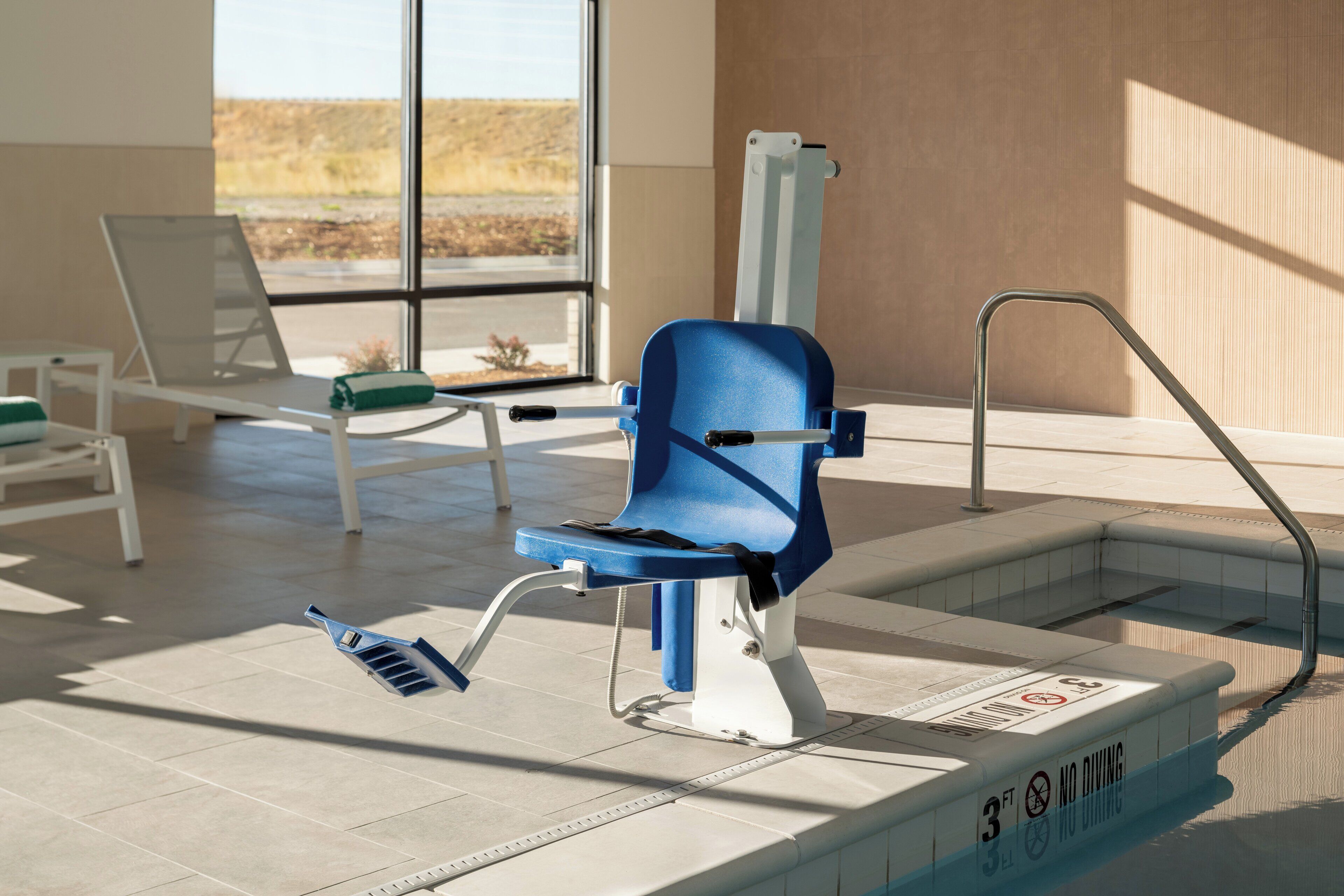 Zona de piscina con una silla azul, una tumbona blanca y una piscina con letrero de no buceo.