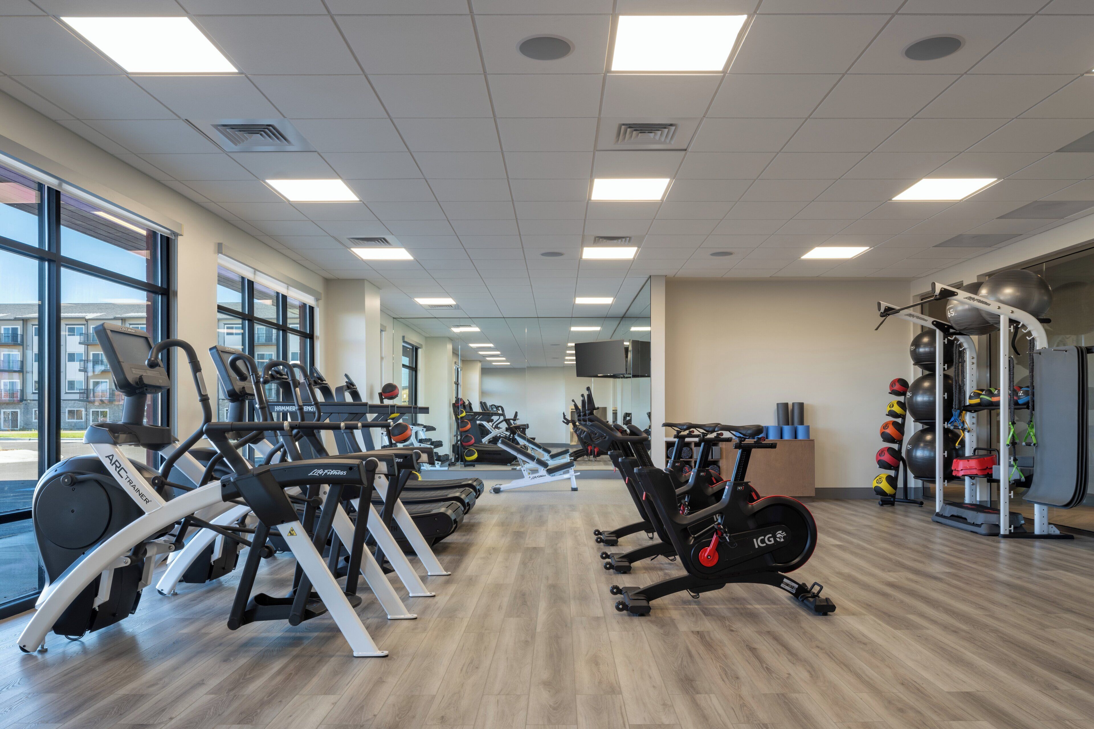 Un gimnasio con máquinas de cardio, equipo de levantamiento de pesas y un espejo grande.