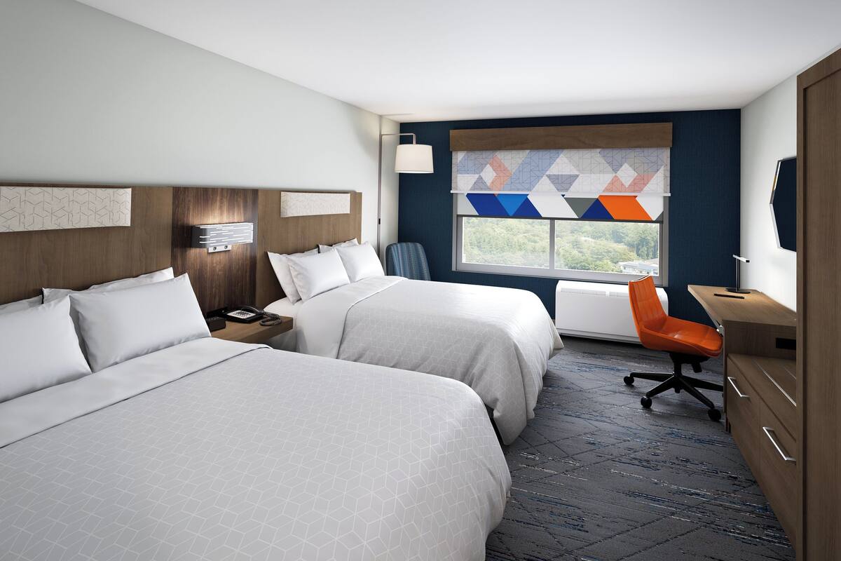 A hotel room with two beds, a desk, a chair, and a window with a view.