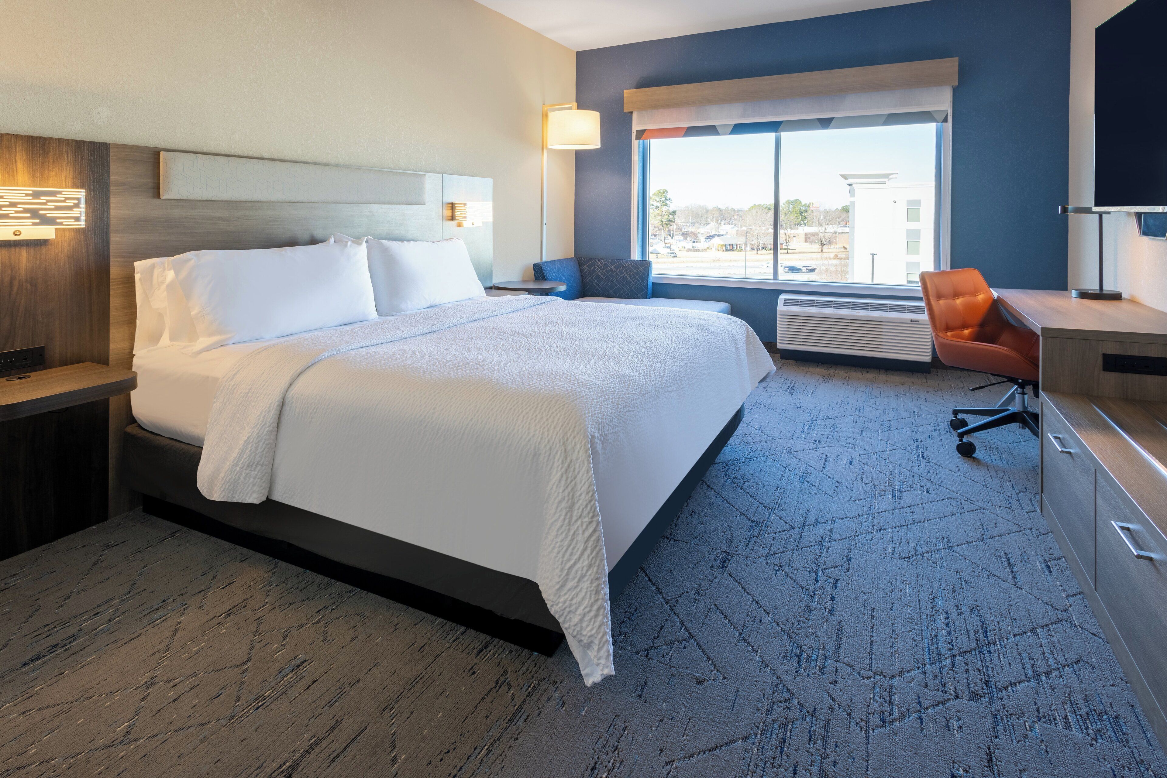 A modern hotel room with a large bed, a desk, and a chair.