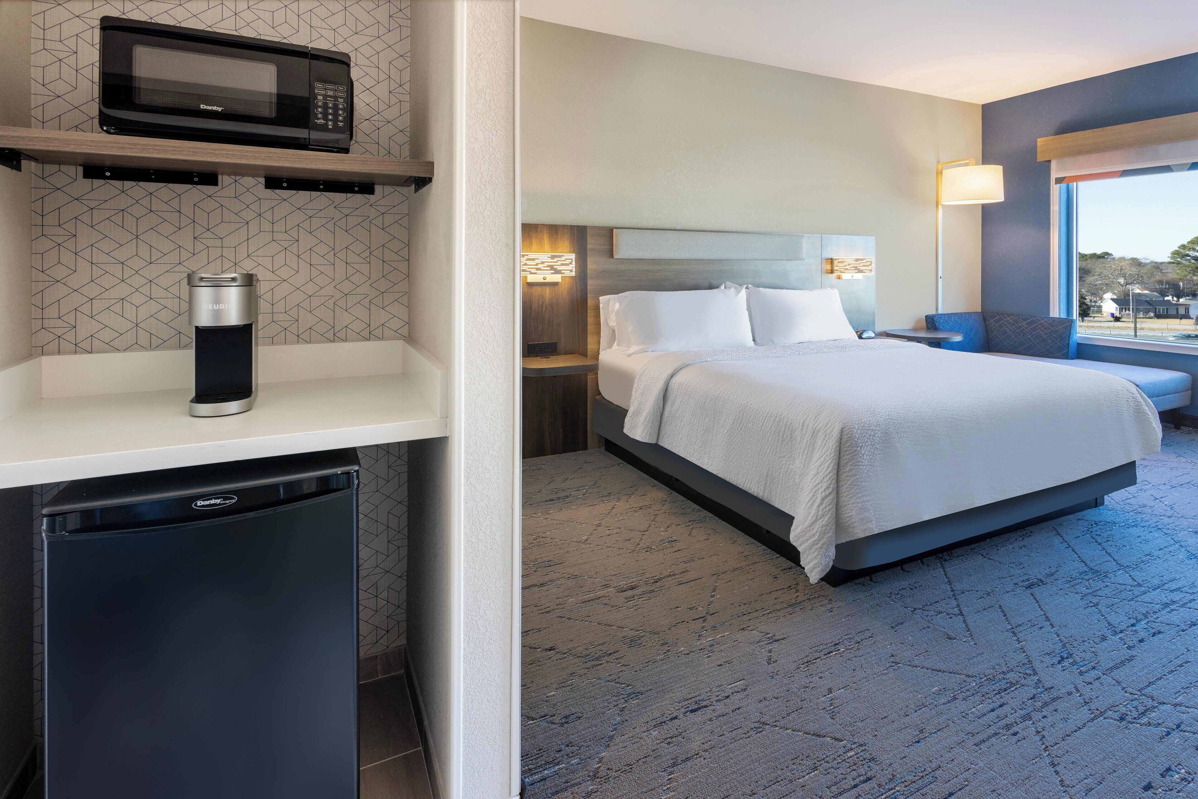 Quarto de hotel com cama, micro-ondas, máquina de café, mesa de cabeceira e janela com vista.