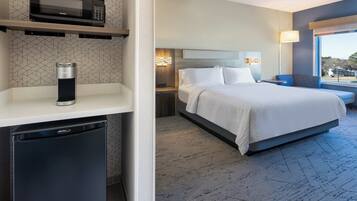 Quarto de hotel com cama, micro-ondas, máquina de café, mesa de cabeceira e janela com vista.