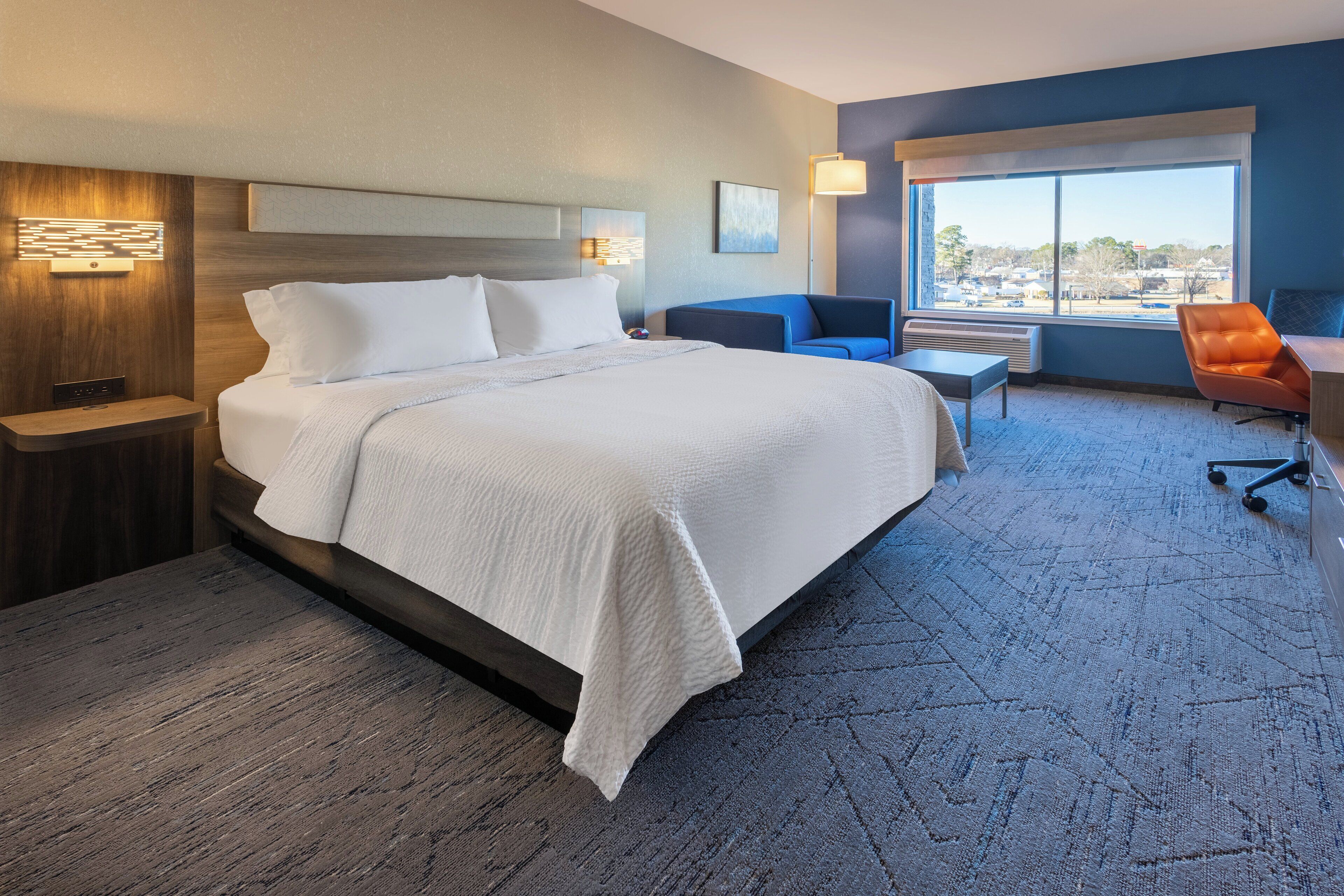 A hotel room with a large bed, a desk, a chair, and a view of the outside.