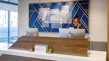 En hotellreception med modern design, med en blå, geometrisk väggpanel och en skylt med texten "Holiday Inn Express & Suites".