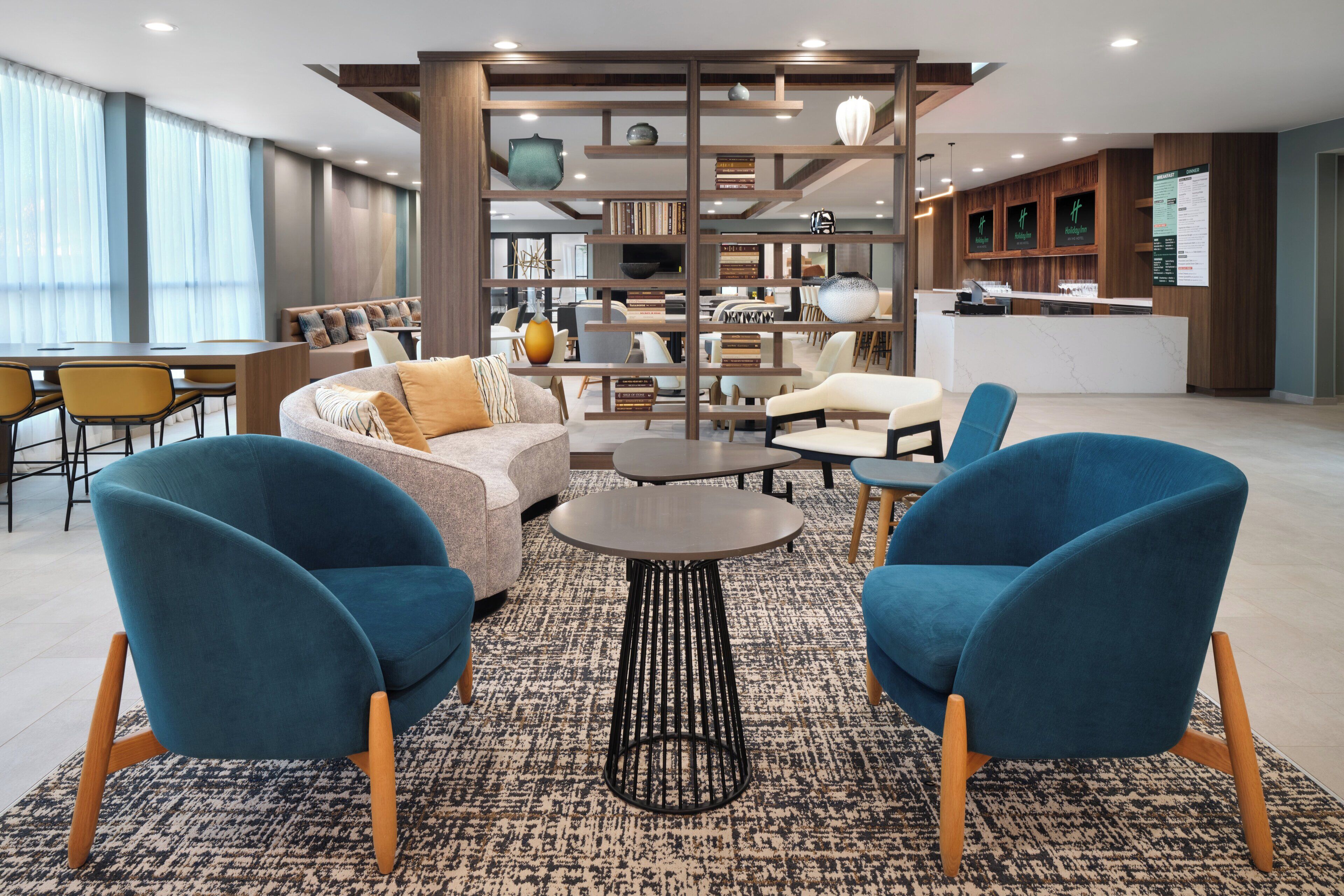Un lobby moderno con un sofá, dos sillones azules, una mesita de centro y una estantería.