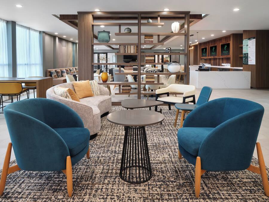 A modern lobby with a sofa, two blue armchairs, a coffee table, and a bookshelf.