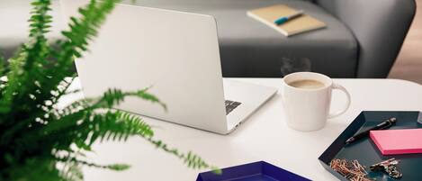 A laptop on a table with a cup of coffee, sticky notes, and keys.