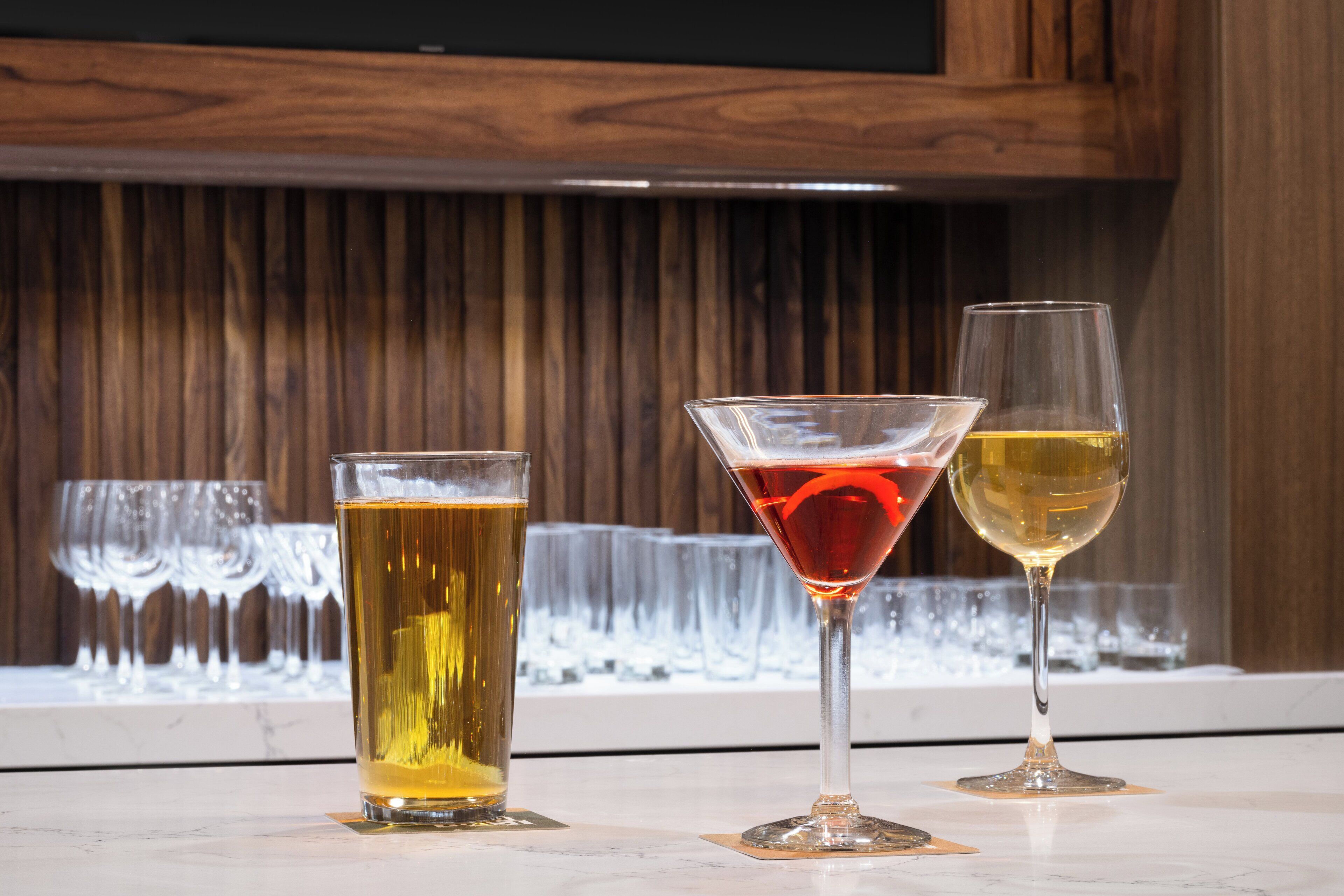 Three glasses of beer and wine on a marble countertop with a wooden background.