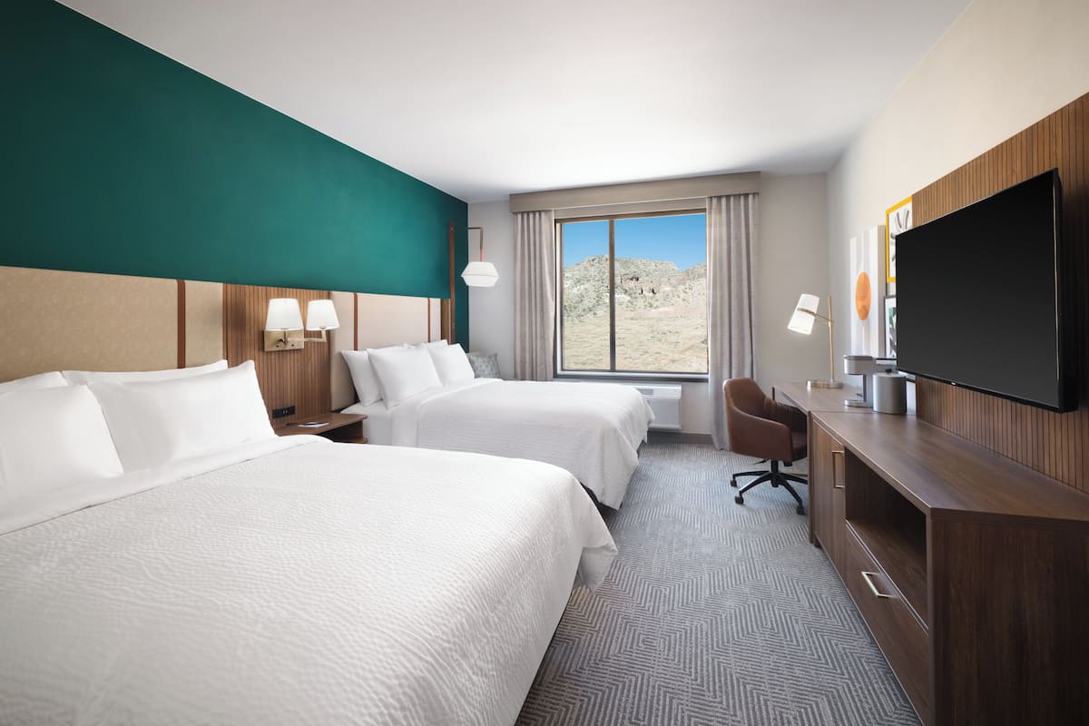 Habitación de hotel con dos camas, un escritorio, televisión y vista al desierto.