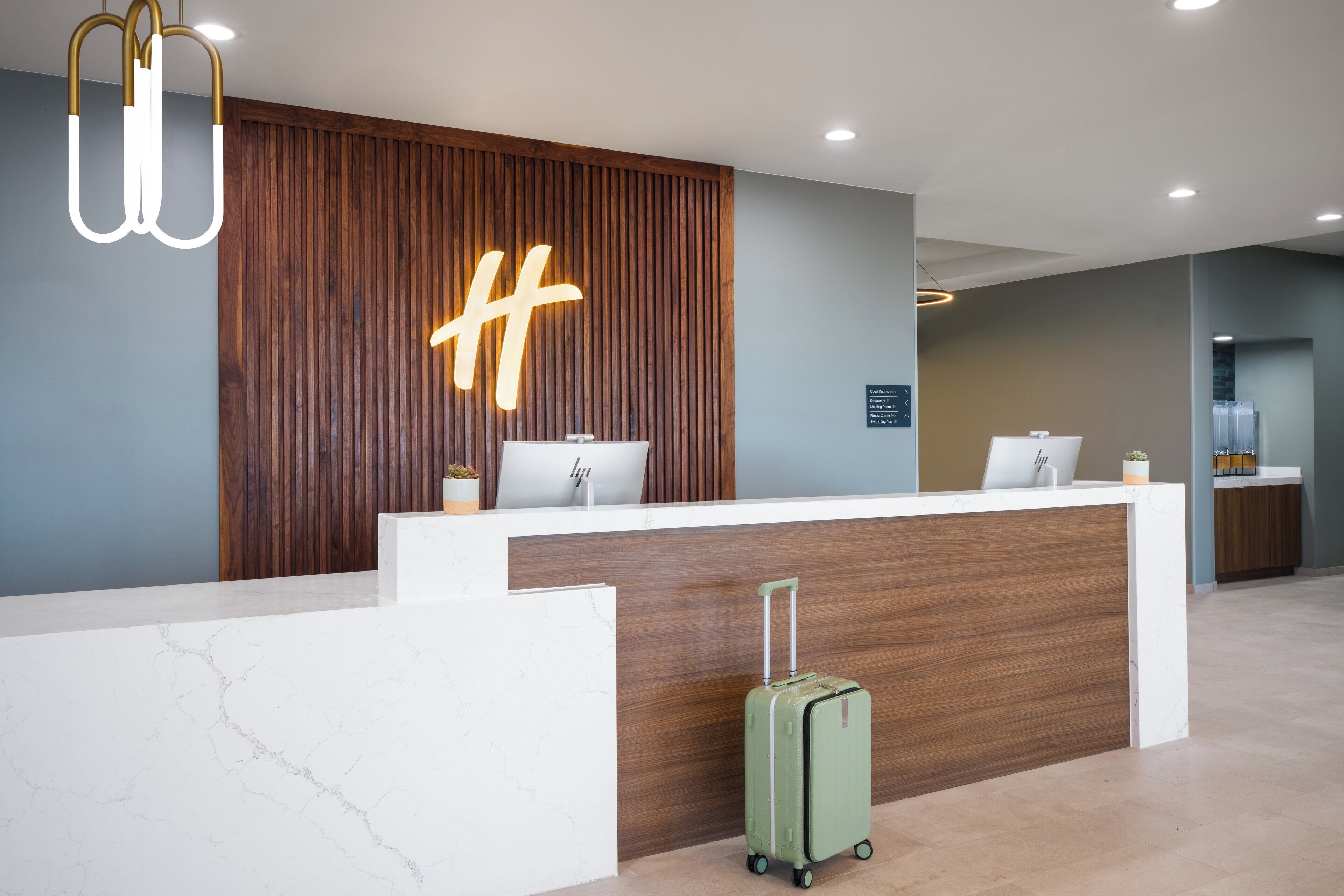 Un comptoir d’accueil moderne, doté d’un panneau de fond en bois et d’un grand panneau lumineux en forme de « H ».