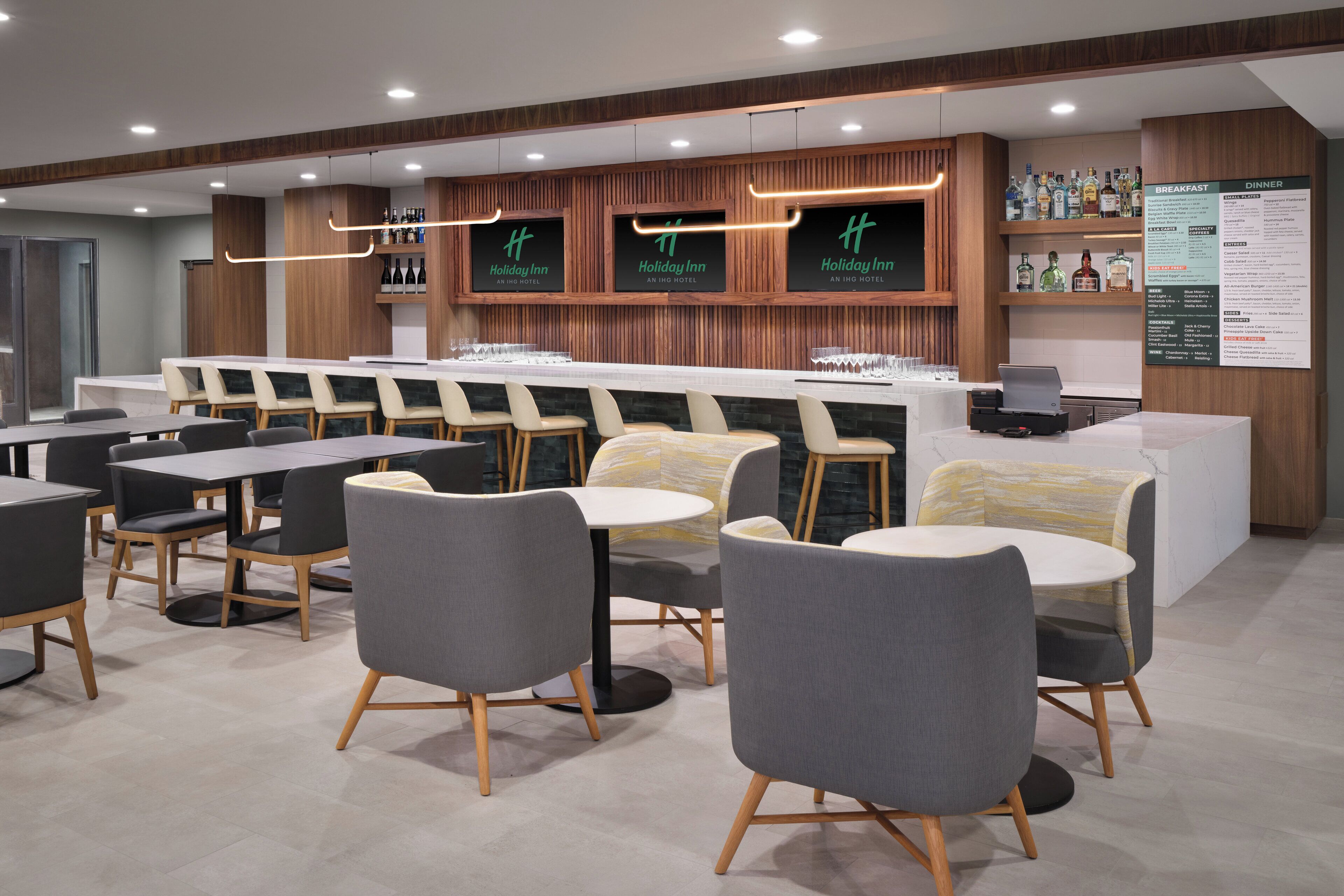 A modern hotel lobby with a bar area, seating arrangements, and a menu board.