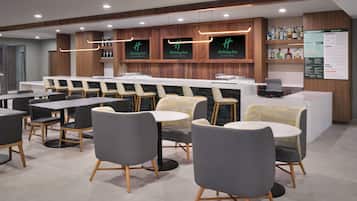 A modern hotel lobby with a bar area, seating arrangements, and a menu board.