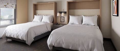 A hotel room with two beds, a window with a view, a nightstand with a lamp, and a framed picture on the wall.