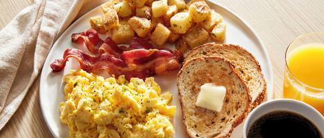 A plate with scrambled eggs, bacon, potatoes, toast with butter, and a glass of orange juice.