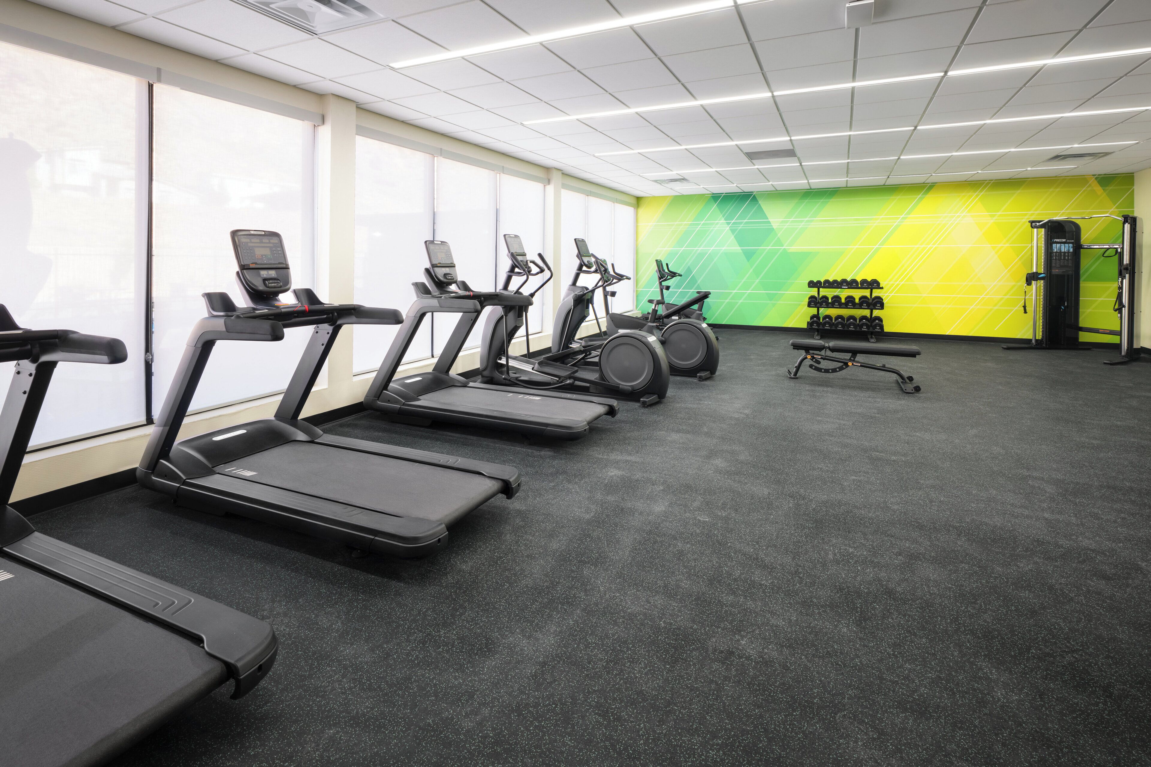 Une salle de sport équipée de tapis de course, de vélos elliptiques et d’un espace dédié à la musculation.