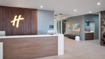 Un área de recepción moderna con un mostrador de madera, un gran letrero iluminado con la letra 'H', una zona de estar con un banco y una obra de arte colgada en la pared.