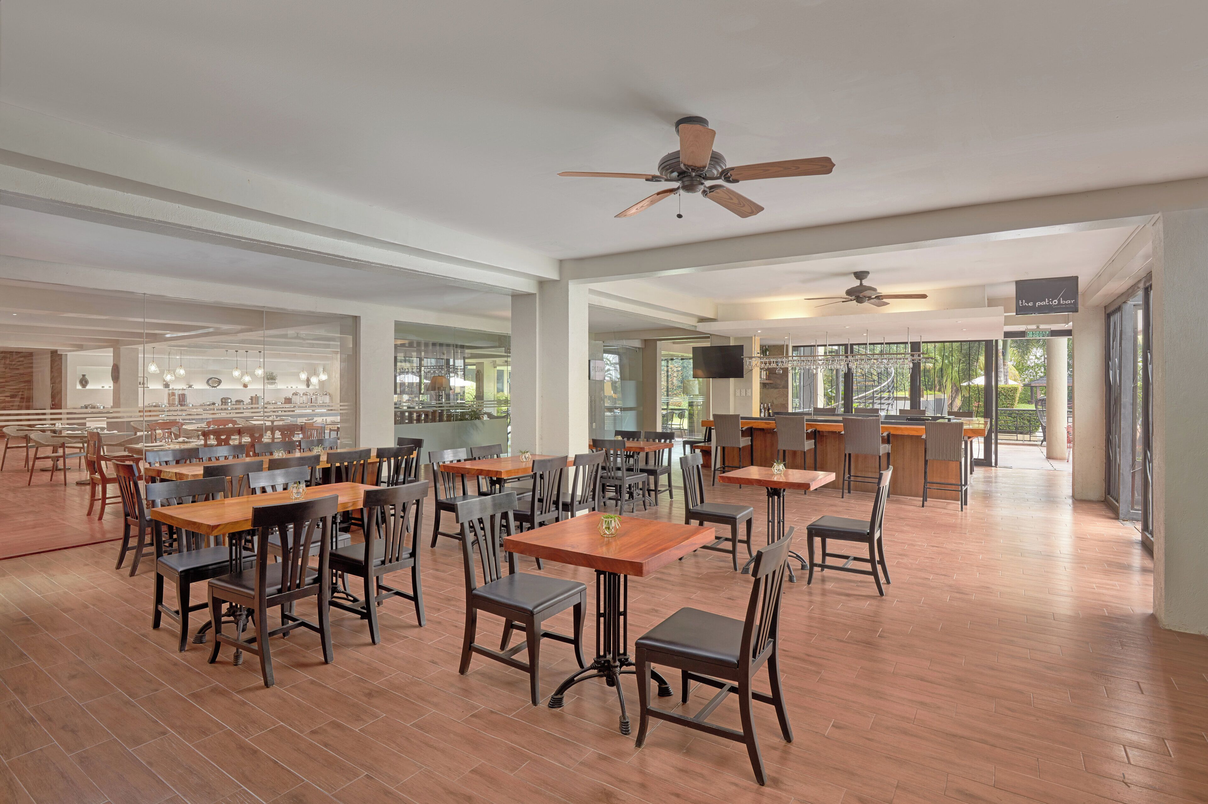 A spacious restaurant with wooden tables and chairs, ceiling fans, and large windows offering views of the outdoors.